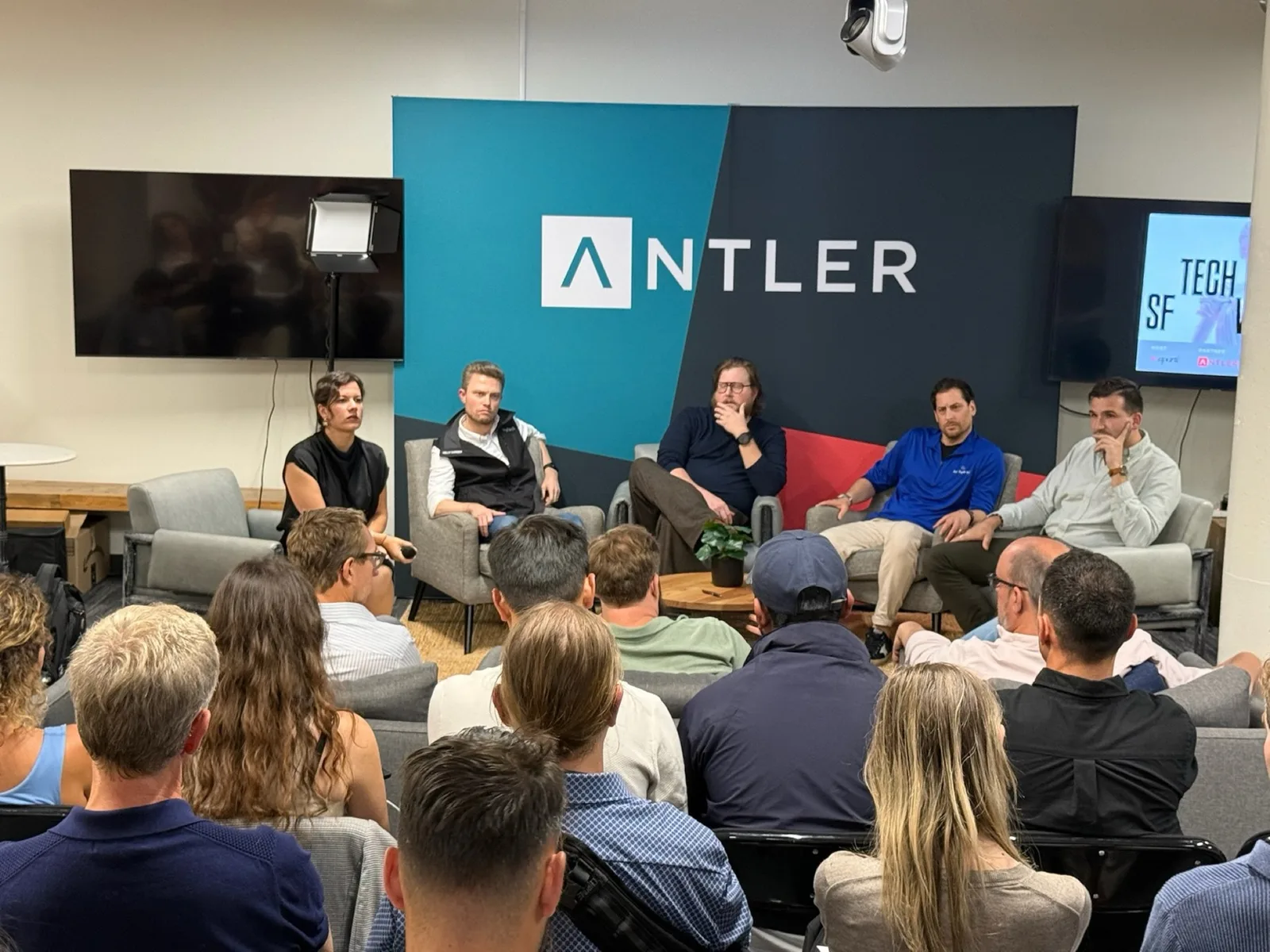 The moderator and four panelists seated in front of a large Antler banner, facing a packed audience.